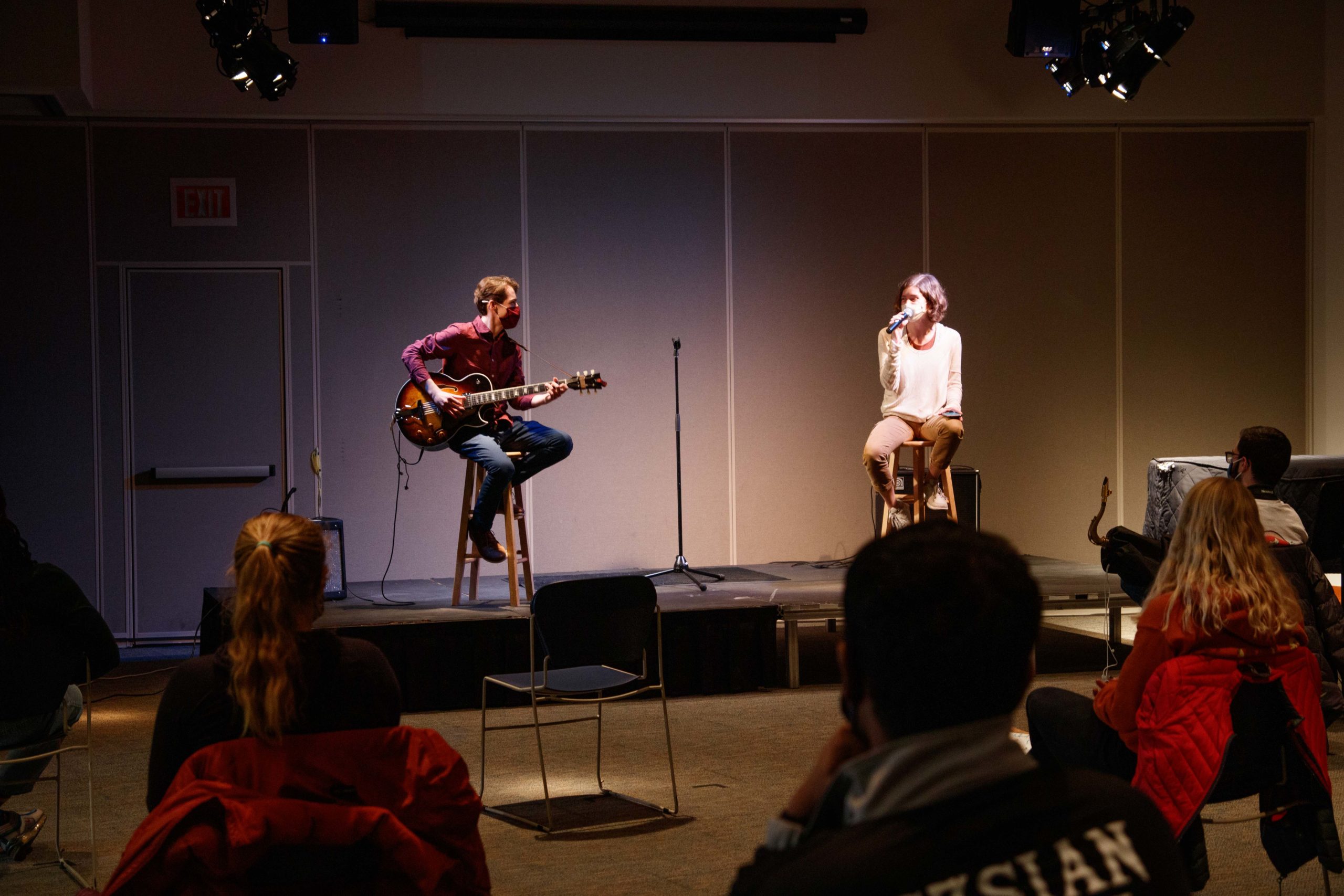 Two musicians, Jackson Peters and Linnea Morris, performing masked and distanced on stage with small audience visible.