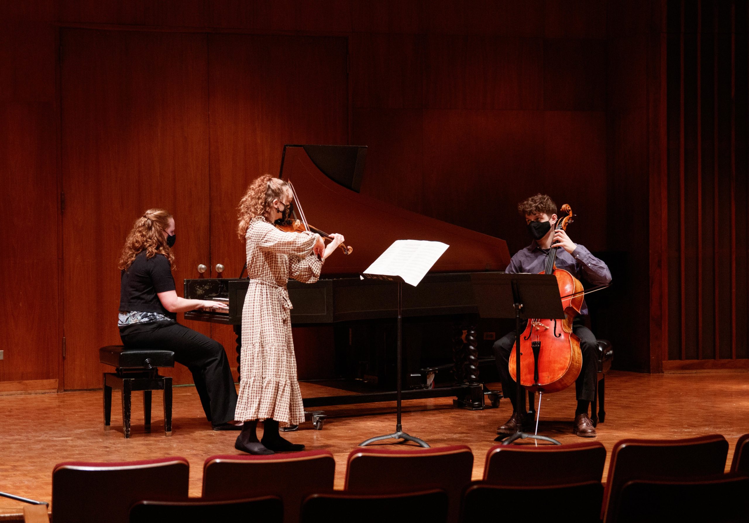 A pianist, violinist, and cellist play together masked on a stage.