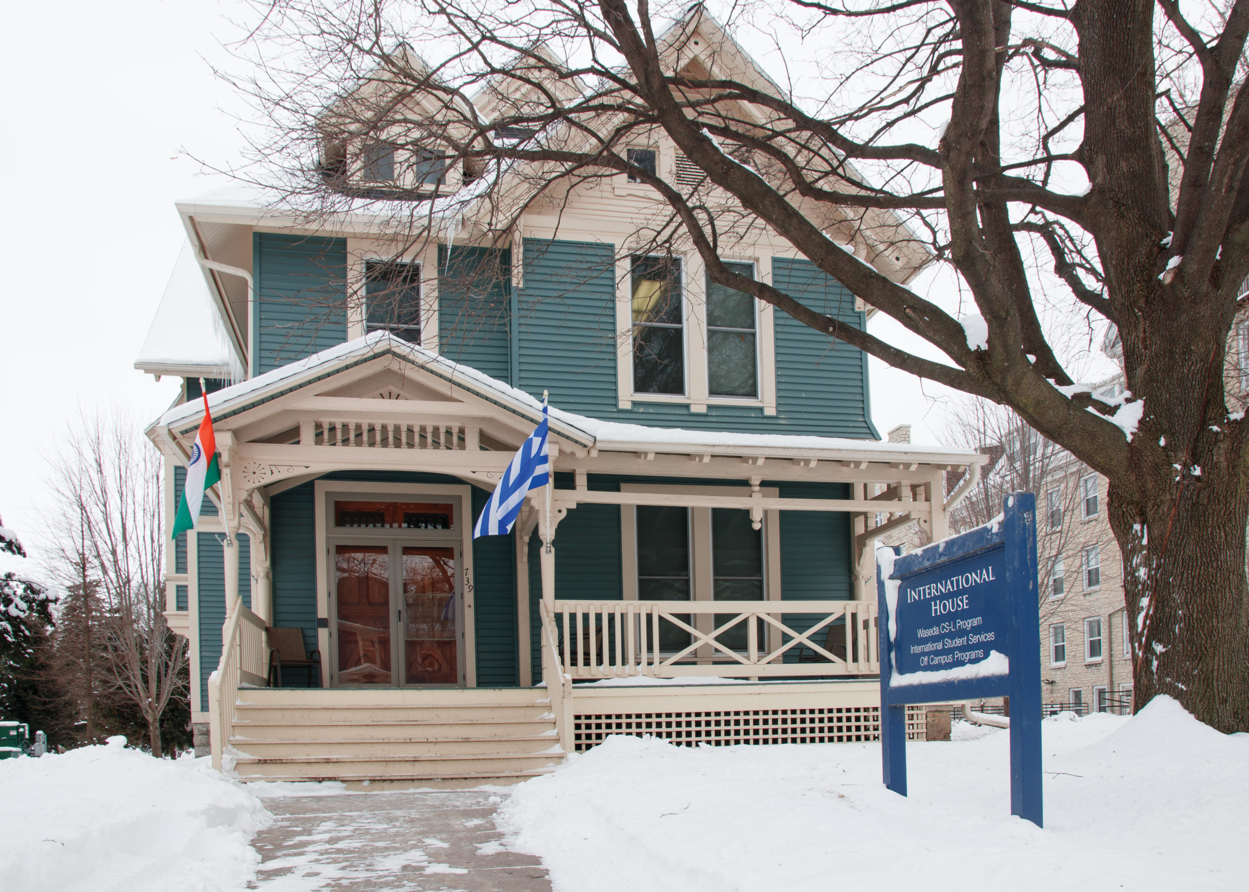 House with two international flags out front and a sign