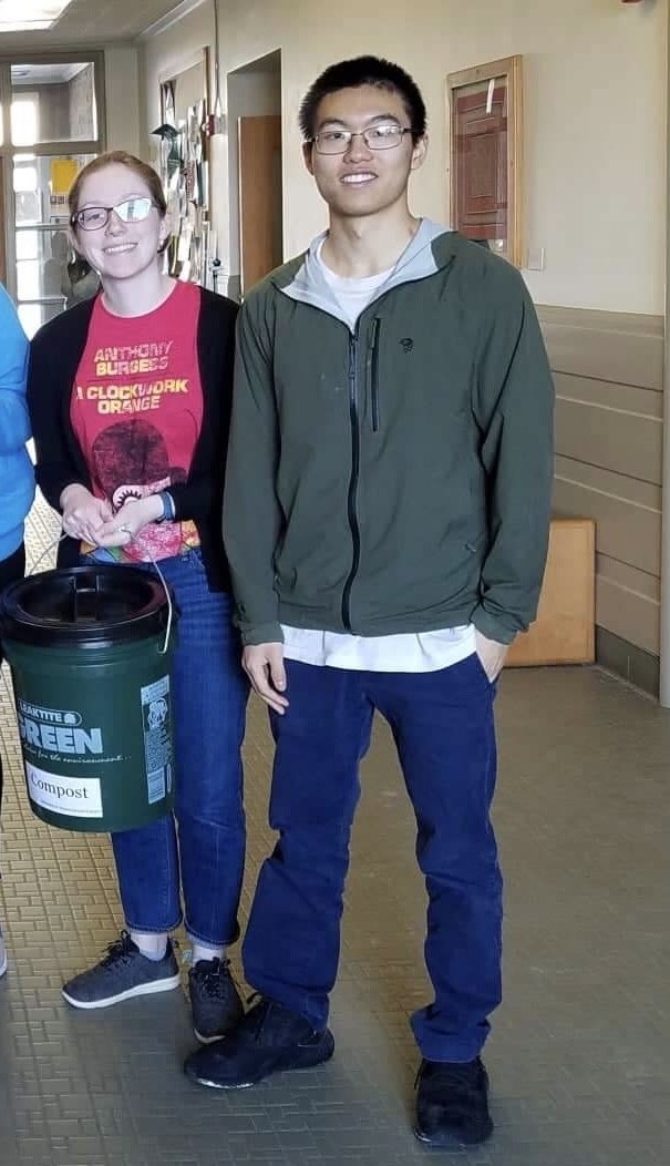 Young woman and man stand in hallway with 5 gallon compost bucket