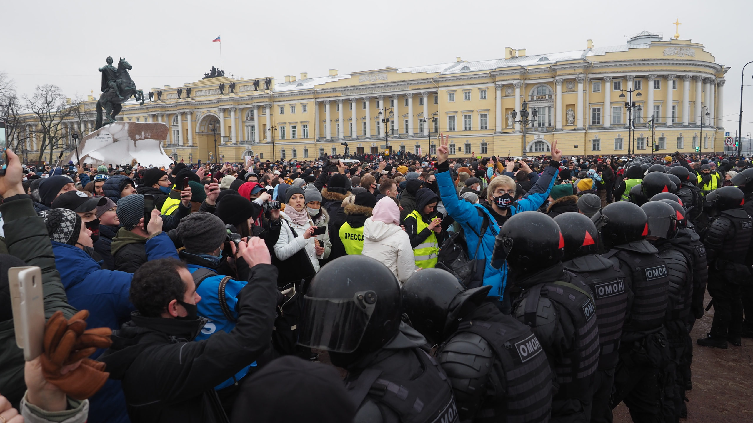 Crowd of protesters and line of police meet in square with large horse statue in background.