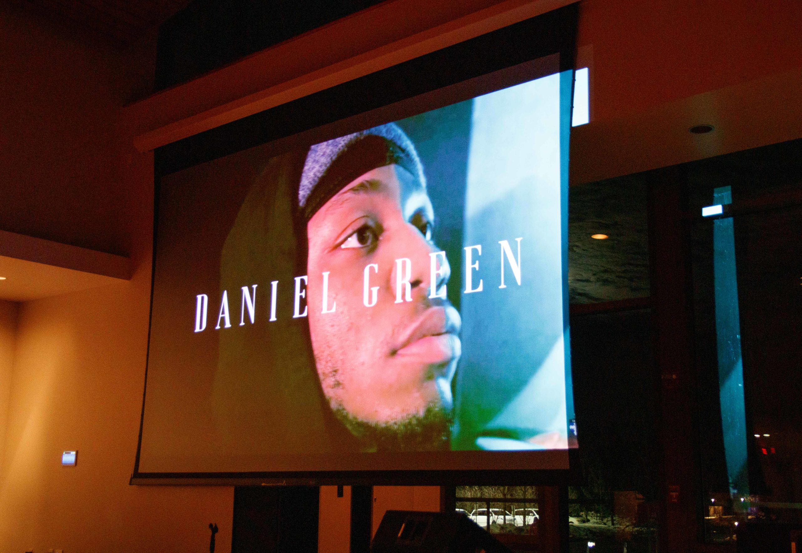 Projection screen with he words "DANIEL GREEN" on them and a young Black man behind the words