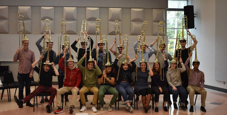 Group of musicians hold their trombones on their heads like hats and pose for a photo.